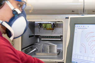 Researcher with a mask looking at screen showing graphs with equipment in the background.