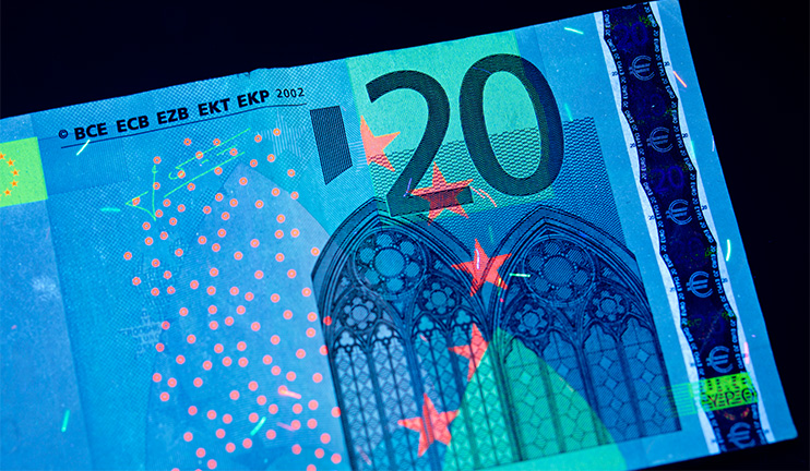 Eine Banknote unter UV-Licht mit leuchtenden Sicherheitsmerkmalen.