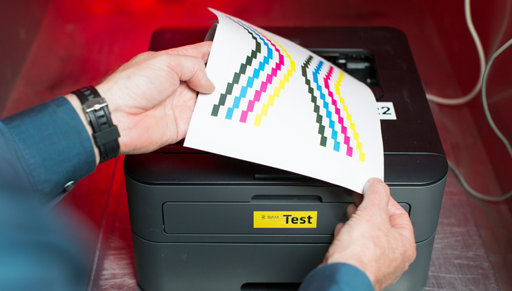 Ein BAM-Mitarbeiter nimmt Testausdrucke aus einem Drucker in der BAM-Emissionsmesskammer Ein BAM-Mitarbeiter nimmt Testausdrucke aus einem Drucker in der BAM-Emissionsmesskammer