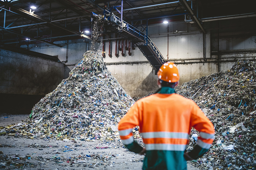 A man in a hard hat and work jacket in a waste recycling plant A man in a hard hat and work jacket in a waste recycling plant