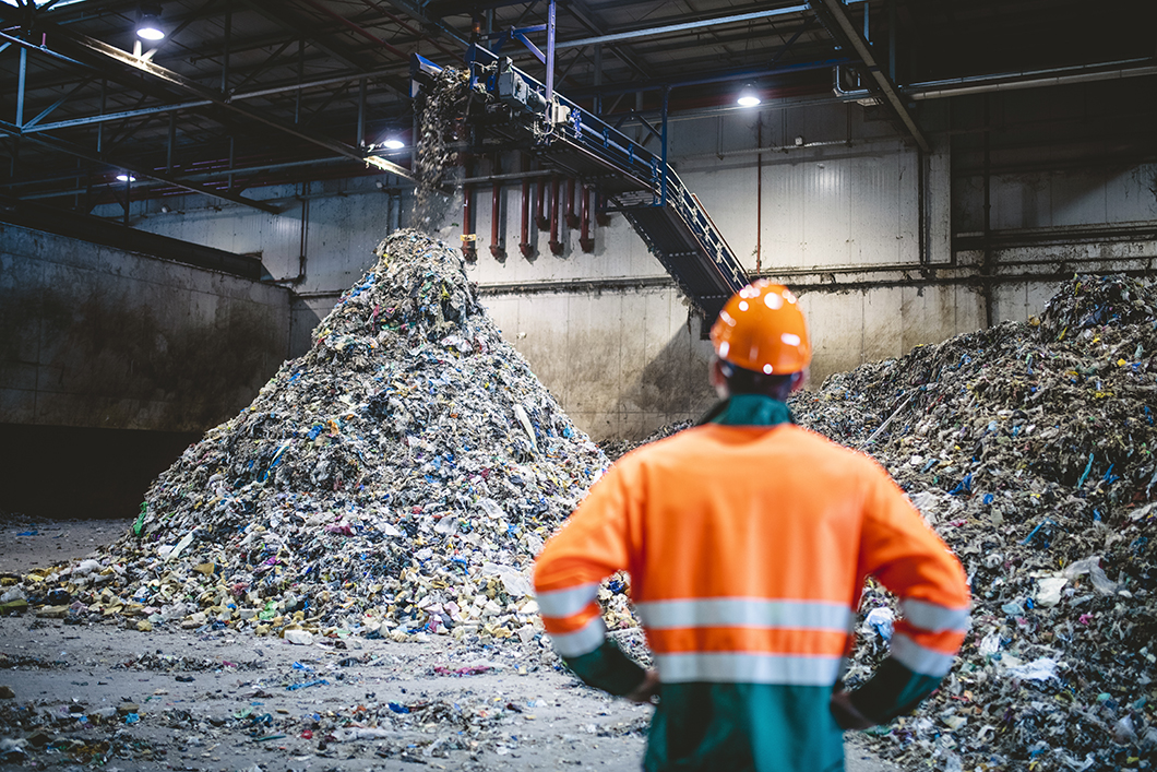 A man in a hard hat and work jacket in a waste recycling plant