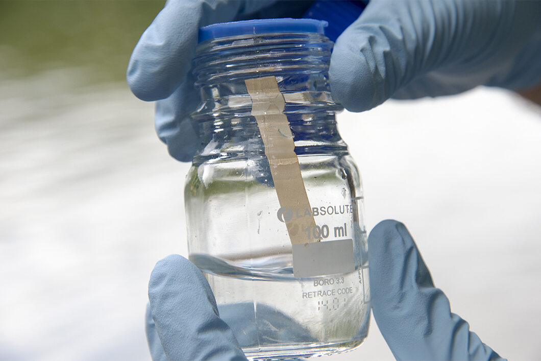 Gloved hands hold a laboratory glass containing a liquid and a test strip. Gloved hands hold a laboratory glass containing a liquid and a test strip.