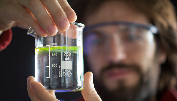 A BAM employee with a glass flask, in which a diesel layer has formed on top of water.