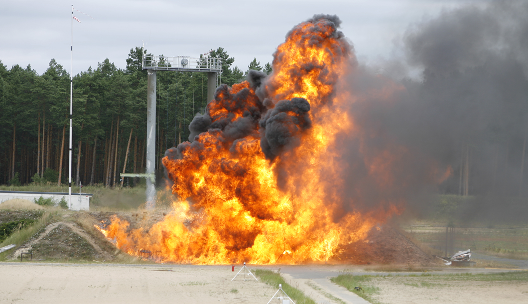 Unterfeuerung der 11 kg Propangasflasche mit Benzin, Flammenausbreitung nach Versagen Die 11 kg Propangasflasche wird mit Benzin unterfeuert. Das führt hier im Versuch zum Versagen des Behälters und Flammenausbreitung.