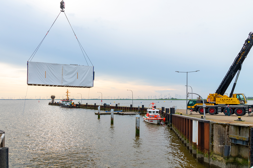 Meerwasserlabor am Eidersperrwerk Ein Kran positioniert den Container, der das Meerwasserlabor behausen wird, am Ufer des Eidersperrwerk.