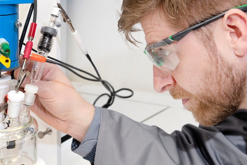 BAM-Forscher*innen wandeln CO2 mithilfe von Bakterien und Solarstrom in nützliche Chemikalien um Forscher mit Schutzbrille vor Versuchsaufbau.